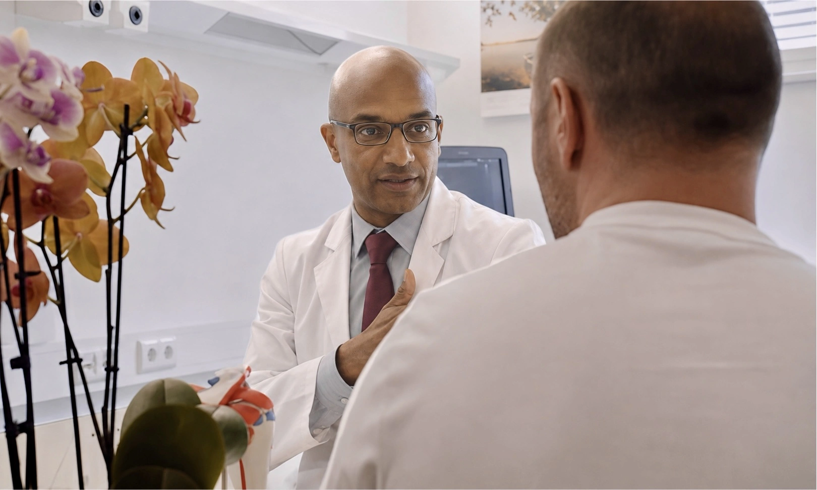 Hamo Kenawy, shoulder surgeon in Dubai, consulting with a patient beside an anatomical shoulder model.